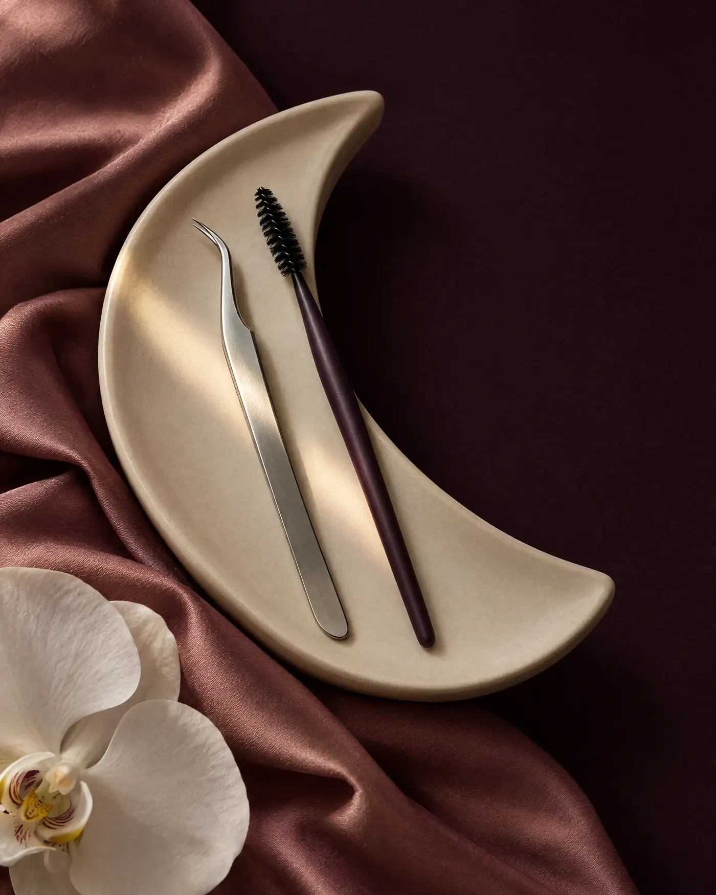 Editorial still life of lash tools on an ivory tray with rose silk